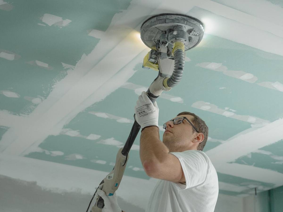 Worker sanding a new ceiling after water damage repair
