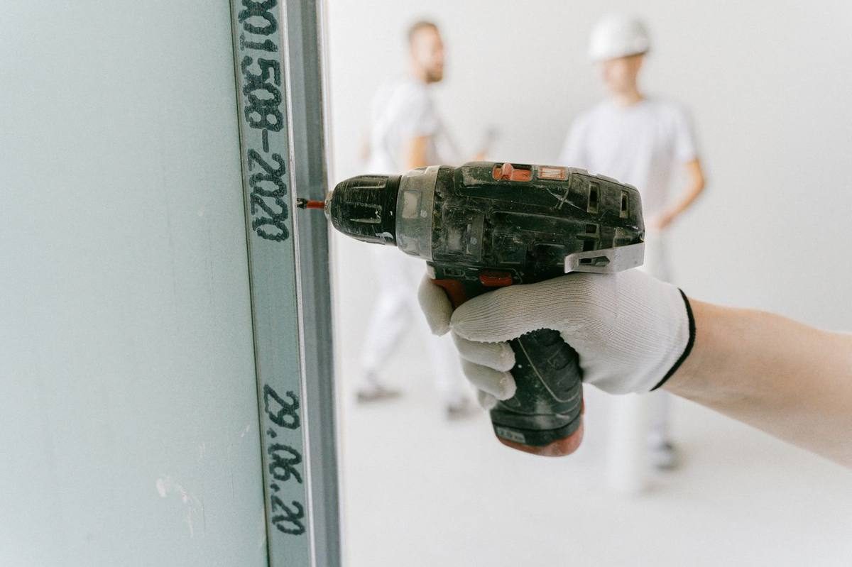 Gloved hand fastening new drywall during repairs