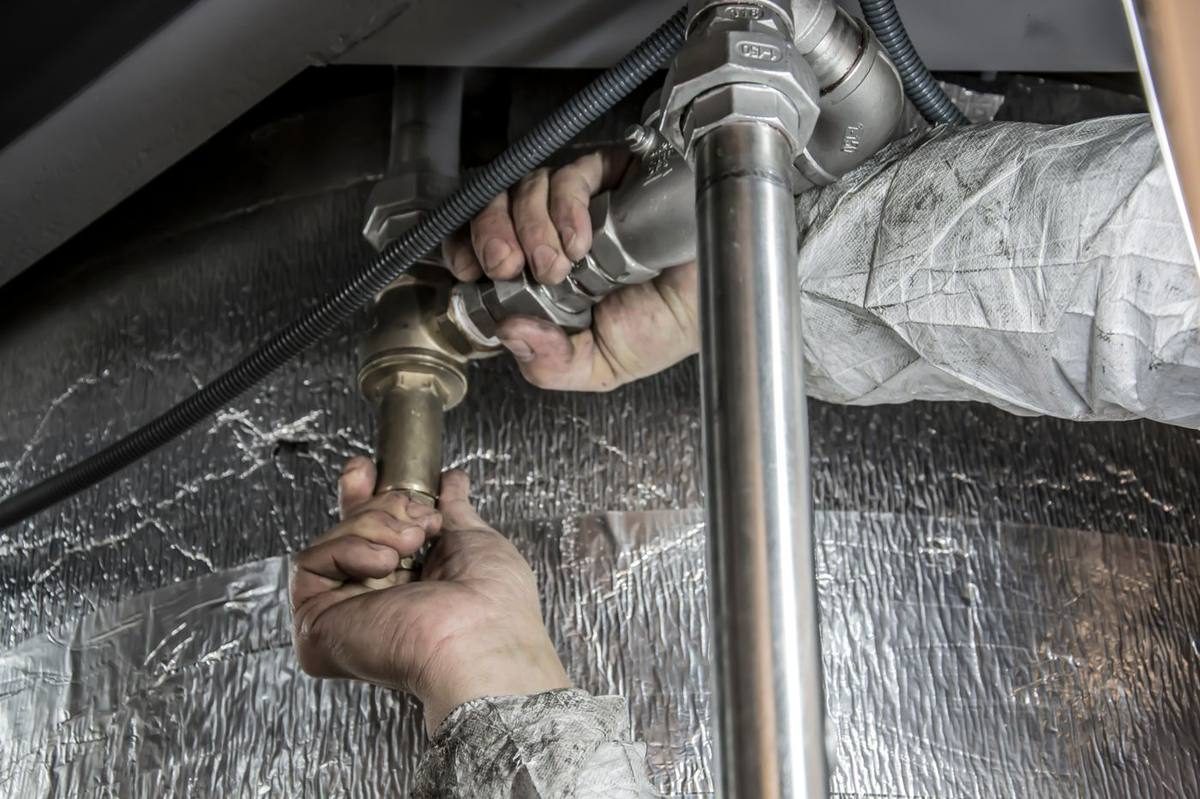Hands repairing a water line next to insulated ductwork