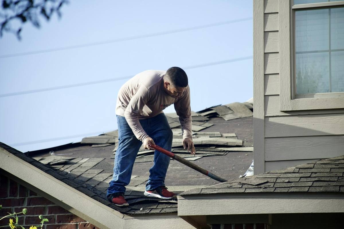Roofer tearing off damaged shingles after a storm